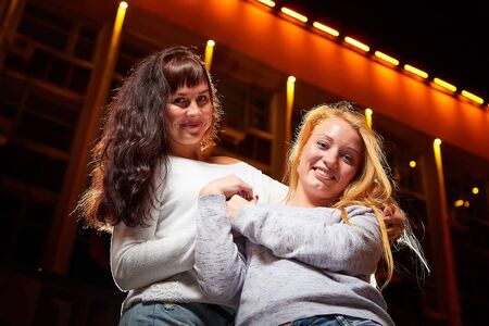 Two female friends on a city street at night. Girls and black background with light outdoors in...