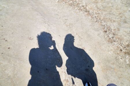 Self-portrait of photographer with camera in hands and other person casting shadow on grey stoney...