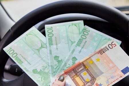 Euro banknotes of various denominations in a woman hand inside of a car and road with nature outside