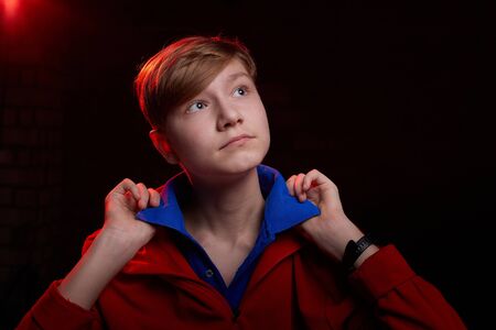 Low key portrait of a handsome brunette young male teenager in sweatshirt or hoodie. Interesting boy and dark background with blue light. Model posing during photoshootの写真素材