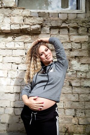Happy healthy pregnancy and maternity. Portrait of pregnant young Caucasian woman wearing long blue dress posing near brick wall building outside. Beautiful hipster girl with big bellyの写真素材