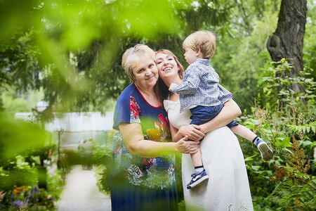 Happy family consisting senior lady grandmother, young mother and small son in garden or park in a summer or autumn dayの写真素材