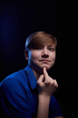 Low key portrait of a handsome brunette young male teenager in blue t-shirt. Interesting boy and...