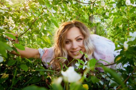 Portrait of a beautiful blonde girl with green eyes and blossoming apple tree with white flower...