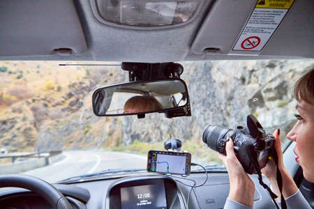 Tbilisi, Georgia - October 19, 2019: Cable of car, steering wheel, dashboard, Navigator, mirror and girl as passanger with camera. Female traveller and photographer on mountains roadのeditorial素材