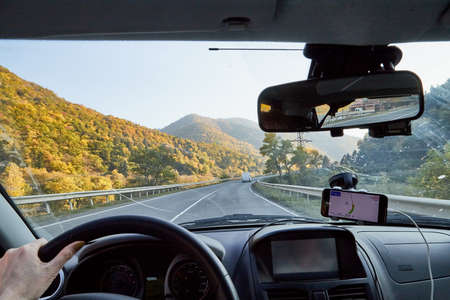 Tbilisi, Georgia - October 22, 2019: Car vindow, hand of woman on steering wheel and view to the road and autumn mountain landscape in a sunny day. Concept alone travel to nature during coronavirusのeditorial素材