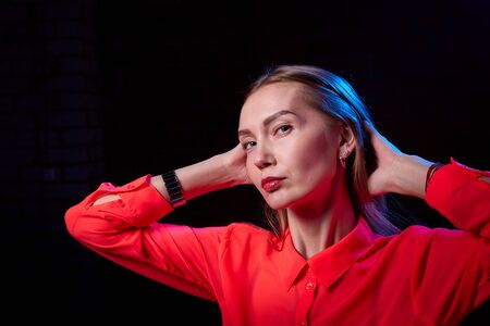 Portrait of elegant woman with long hair in red dress and dark background with blue light. Model posing doring studio photo shotの写真素材