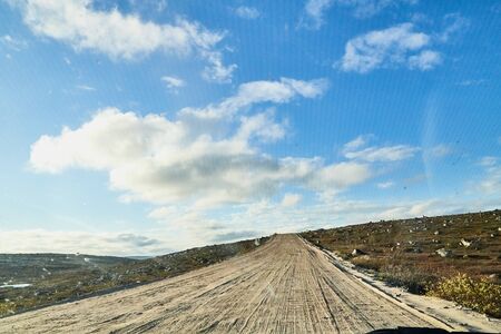 View from car windscreen with stripe relief to dirt country road, tundra and blue sky with white clouds in norht region at a nice sunny dayの写真素材