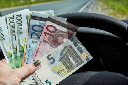 Euro banknotes of various denominations in a woman hand inside of a car and road with nature outsideの写真素材