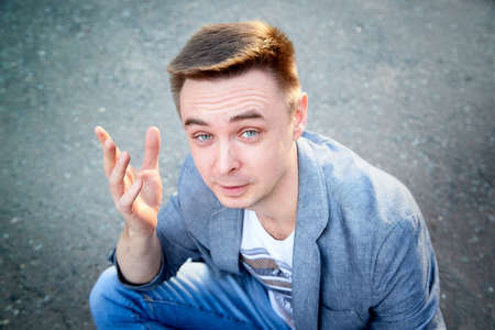 Kirov, Russia - September 04, 2019: Portrait of a handsome fun man sitting on the asphalt on a city street in a summer, spring or autumn dayのeditorial素材