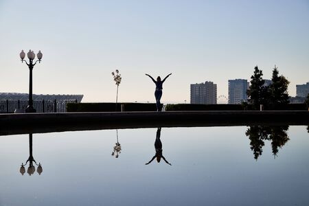 Silhouette girl or woman far away near water in city park. Female traveller posing near lake in autumn, spring or summer dayの写真素材