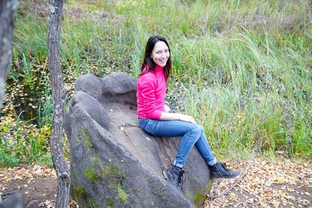 Beautiful young woman sitting on the big stone in the forest with sprice in autumn dayの写真素材
