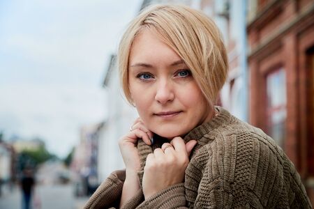 Blonde girl near near the facade of a large red brick building with windows in the Central part of the ancient city. Walk in downtown. Portrait of a funny pretty girl on the street of the townの写真素材
