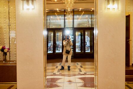 A beautiful hall with white columns and a mirror that reflects a girl photographer with a cameraの写真素材