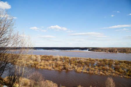 High water on a river or on a lake in sunny spring day. Russian nature landscape with water, trees and blue sky with white cloudsのeditorial素材