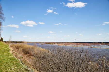 High water on a river or on a lake in sunny spring day. Russian nature landscape with water, trees and blue sky with white cloudsのeditorial素材
