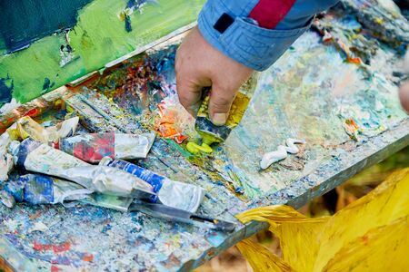 Male hand of artist, palette with paints and canvas in nature outdoors and greenery background in a summer sunny dayの写真素材