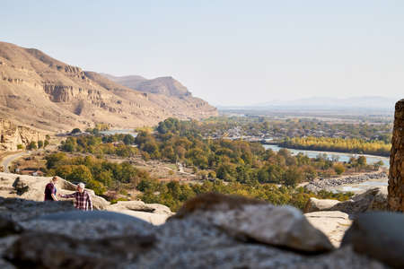 Uplistsikhe, Georgia - October 22, 2020: Tourists in a mountain reserve near ancient old city with rocks, residential and religious caves and blue sky on Sunny summer day. Uplistsikhe city in Georgiaのeditorial素材