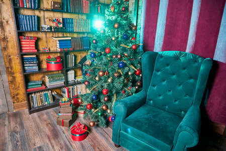 Kirov, Russia - November 09, 2019: Vintage interior with chair, bookcase with books, Christmas tree with toys,gifts, garlands and other Christmas decorationsのeditorial素材