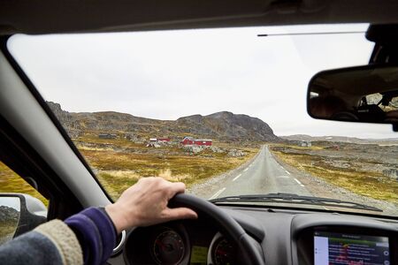View from car window on the road and pity strange landscape with a mountains, rocks and cloudy sky and hand of woman. Landscape through windscreen in Norway. Single trip for isolation in a coronavirusの写真素材