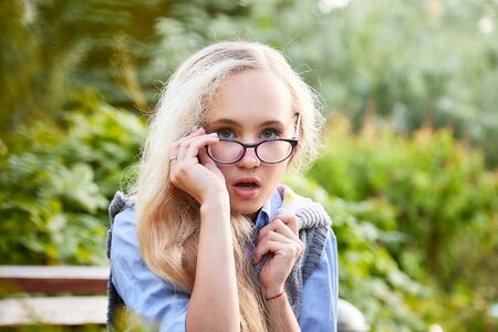 Pretty teenage girl 14-16 year old with curly long blonde hair and in glasses in the green park in a summer day. Beautiful outdoors portraitの写真素材