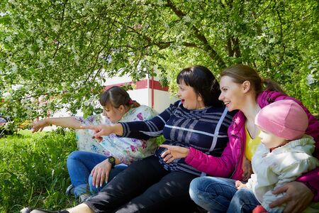 Three different funny women and one small seriously girl in the park full of apple blossom trees in...