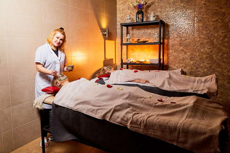 Kirov, Russia - February 25, 2019: Nurse making a Spa mud mask on a girl's face in a salon or room with a couch, white towels and a beautiful light. Woman relaxing during spa treatmentsのeditorial素材