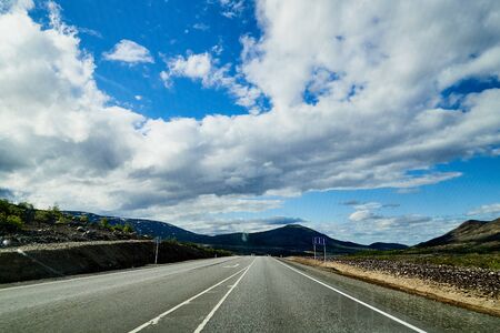 View from car windscreen with stripe relief to highway, tundra and blue sky in norht region at a...