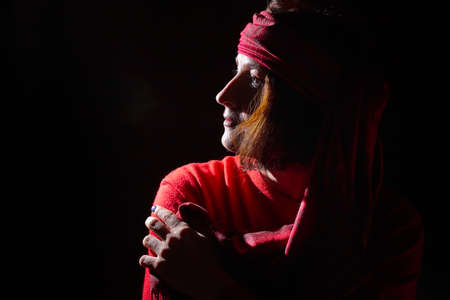 Portrait of middle age woman in red sweater and the turban of a wizard or sorcerer on black background. Actress in a magical, fantastic, fairy-tale movie. Female model posing at dark studio with flashの写真素材