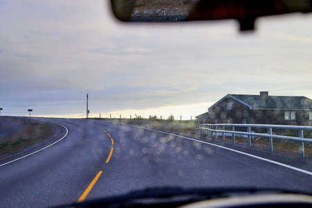 Rain drops on car glass in rainy day and road background. Travel in a cloudy evening or morningの写真素材