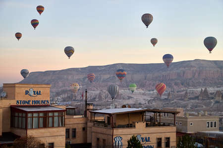 Cappadocia, Turkey - December 20, 2019: Hot air balloons flying in blue sky with white clouds over homes of city Goreme at morning during sinrise. Great interesting attraction for touristsのeditorial素材