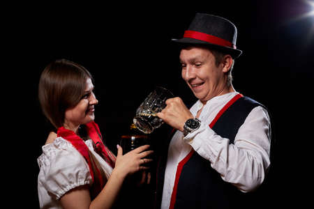 Girl pouring beer from a keg into a mug of guy in Octoberfest. Couple in nationa ethnic dress having...