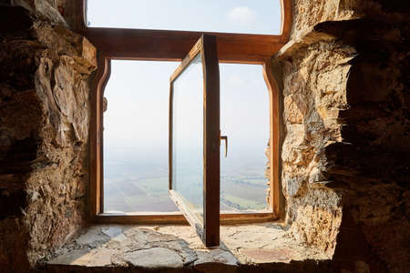 Wooden window in the stone wall and a view of the green valley with fog belowの写真素材