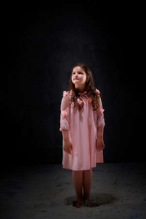 Small girl in white dress in dark studo before photoshoot with flour. Young model posing with white dust and black background.の写真素材