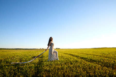 Beautiful woman or girl with magnificent figure and plastic movements walking and dancing in green field with trimmed grass in the setting sun during sunset with warm yellow lightの写真素材