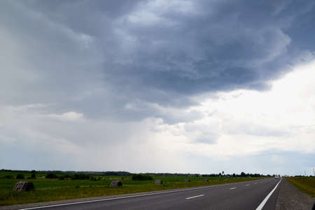 Beautiful landscape with blue sky, white clouds and the road that goes to the horizon through fieldの写真素材