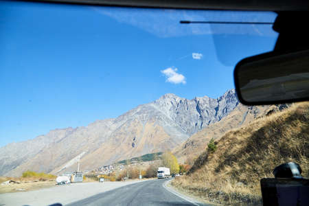 Tbilisi, Georgia - October 25, 2019: Car vindow, hand of woman on steering wheel and view to the road and autumn mountain landscape in a sunny day. Concept alone travel to nature during coronavirusのeditorial素材