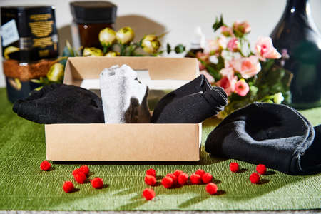 Several pairs of new male cotton socks with a brown cardboard box on a green surface and flowers...