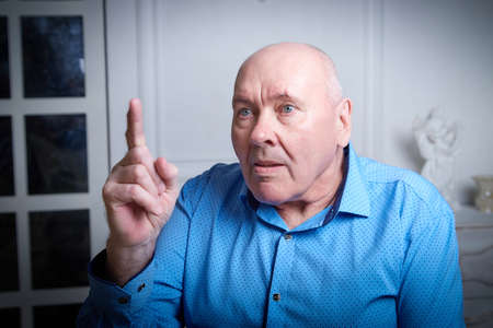 Portrait of an elderly bald man in a blue shirt in the room. A poor pensioner lives aloneの写真素材
