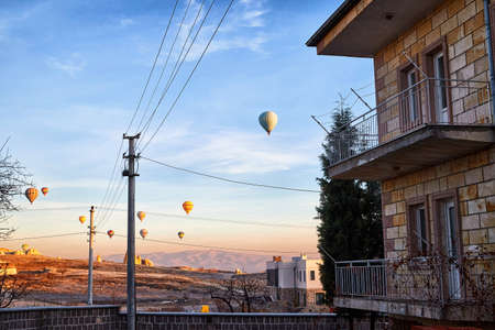 Cappadocia, Turkey - December 20, 2019: Hot air balloons flying in blue sky with white clouds over homes of city Goreme at morning during sinrise. Great interesting attraction for touristsのeditorial素材