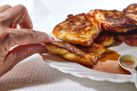 Pancakes on white plate and sweet liquid honey or caramel with a small spoon, woman hand and with...