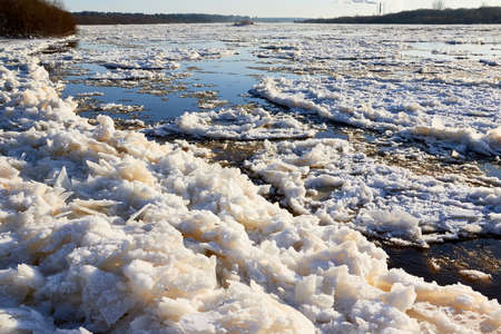 Ice drift on a river with blue high water and big water, white snow broken ice full of hummocks in it and sun reflection in sunny spring dayの写真素材