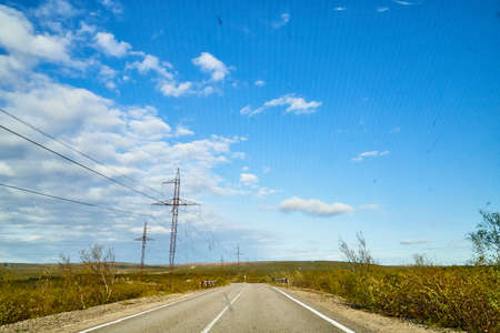View from car windscreen with stripe relief to highway, tundra and blue sky in norht region at a nice sunny dayの写真素材