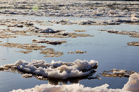 Ice drift on a river with blue high water and big water, white snow broken ice full of hummocks in it and sun reflection in sunny spring dayの写真素材