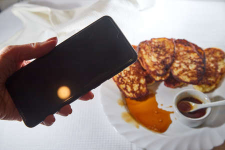 Pancakes on white plate, sweet liquid honey or caramel with a small spoon and taking pictures on...