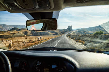 View from car window on the road and strange landscape with a valley, mountains and blue sky with...