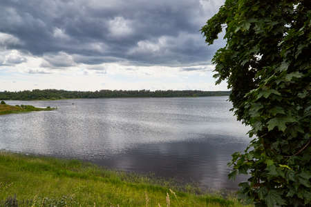 View of the lake water from the coast with trees and greenery, the horizon and blue sky with white...