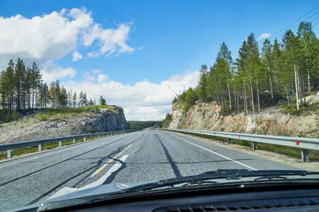View from car window on the road and landscape with forest, tees, and blue sky with clouds. Landscape through windscreen with a relief. Trip for isolation in a coronavirusの写真素材