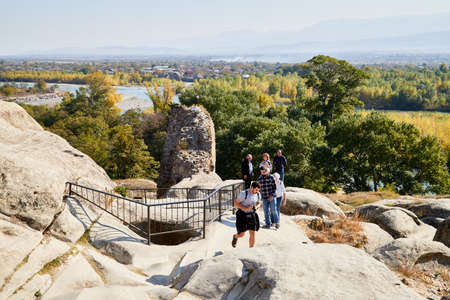 Uplistsikhe, Georgia - October 22, 2020: Tourists in a mountain reserve near ancient old city with rocks, residential and religious caves and blue sky on Sunny summer day. Uplistsikhe city in Georgiaのeditorial素材