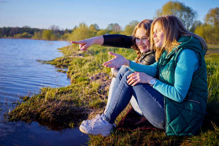 Two girls friends, sisters, cousins socializing and having fun on the shore or beach of a lake or riverの写真素材